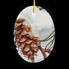 Close up of Snow Cone oval ceramic ornament. It features a closeup of a pine cone with snow on it.