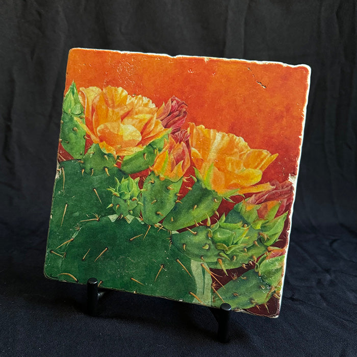 The "Abundance" trivet featured on its iron stand. The image is a watercolor painting of a prickly pear in bloom.