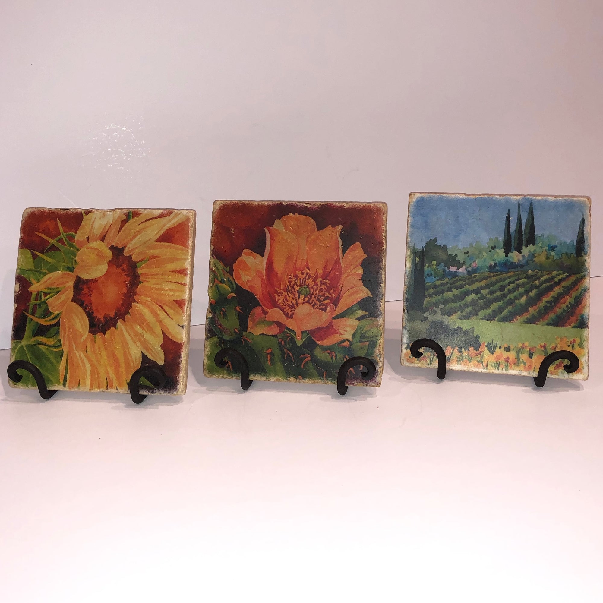 Prickly Pear 2, Sunflower 1, and Vineyard I trivets are shown in iron stands.